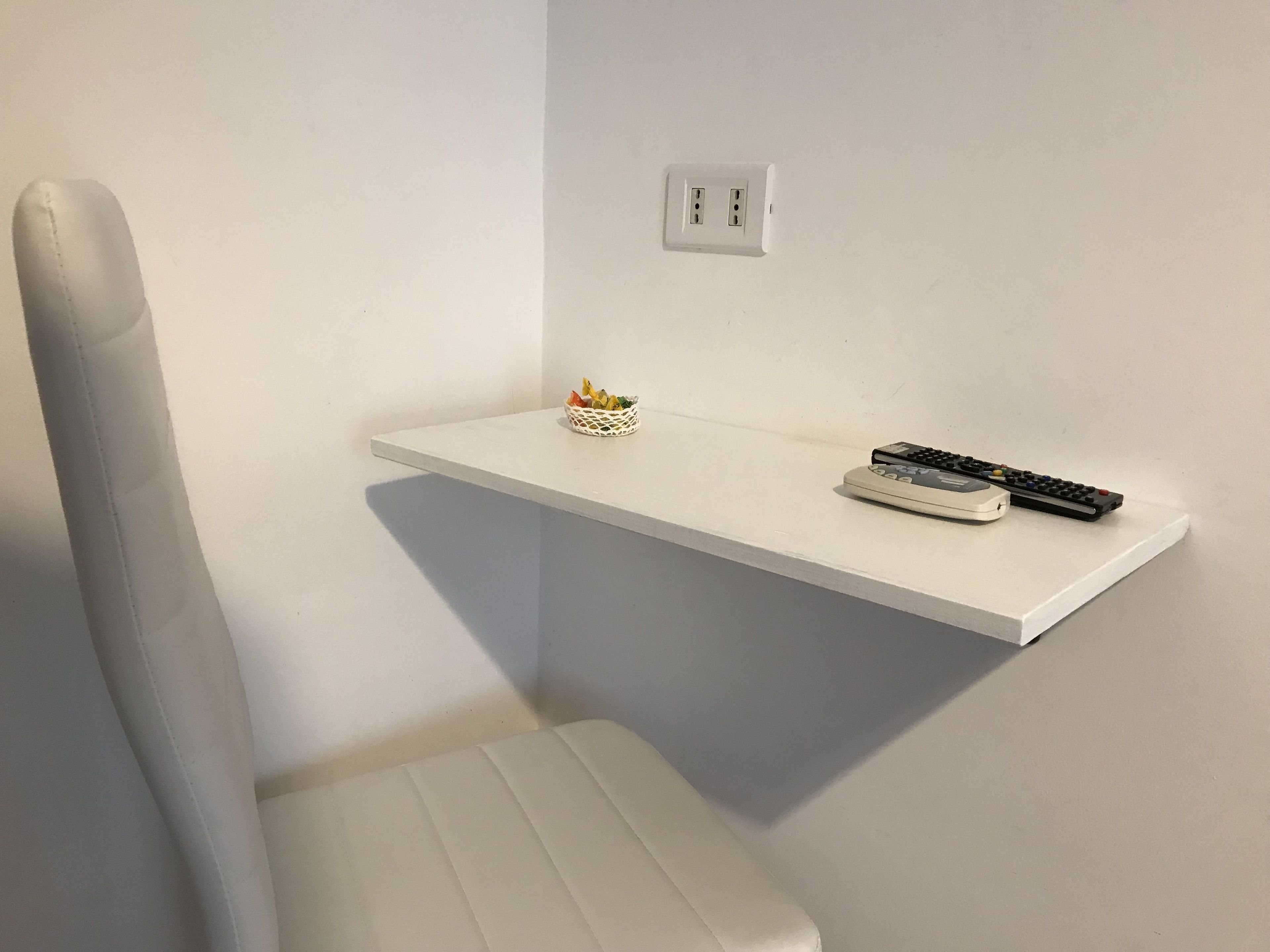 Pared branca com prateleira branca que exibe uma cesta de frutas e dois controles remotos.