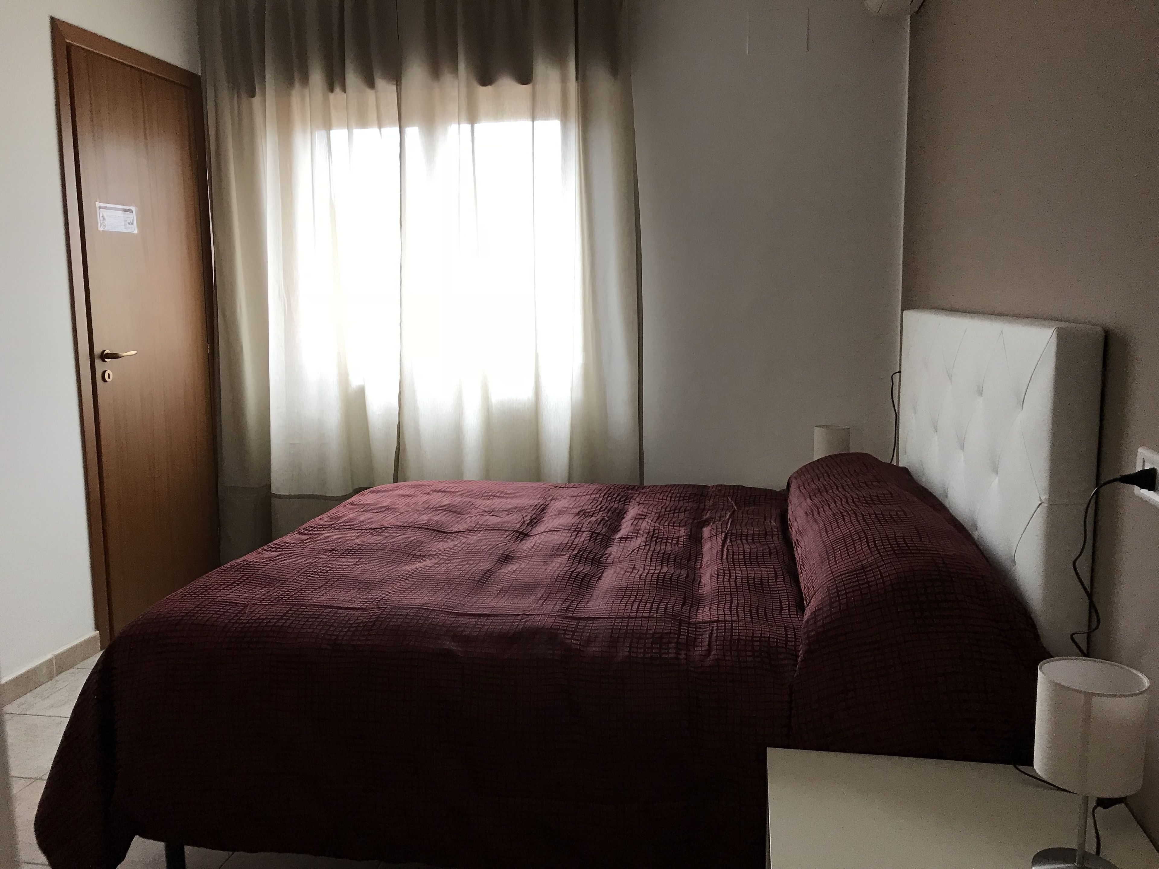 A bedroom with a bed, curtains, a door, and a bedside lamp.