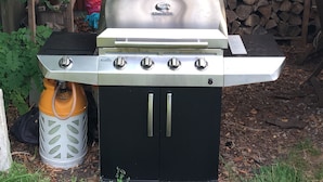 Un barbecue à gaz Char-Broil doté de quatre brûleurs, d’un meuble noir et d’une bouteille de gaz.
