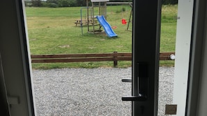 On aperçoit un terrain de jeux avec un toboggan et des balançoires à travers une porte.