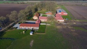 Une vue aérienne d’une ferme comprenant plusieurs bâtiments, notamment des granges et des habitations, entourée de champs et d’arbres.