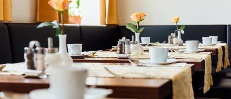 A restaurant with multiple tables set for dining, each with a vase of flowers, salt and pepper shakers, and white cups and saucers.