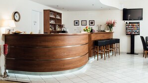 Et hotellets reception område med en træreception, et ur og et vægmonteret fjernsyn.