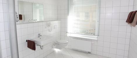 A modern bathroom with a glass shower enclosure, a white sink, a toilet, and a window with blinds.