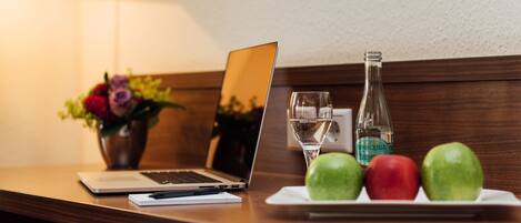 Una laptop sobre una mesa de madera con una botella de agua, un vaso y manzanas.