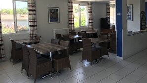 Comedor con mesas y sillas de mimbre, ventanas amplias con cortinas, un radiador y una encimera con televisor.