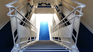 Escalera de un hospital o centro médico, con barandillas blancas, alfombra azul y obras de arte en las paredes.