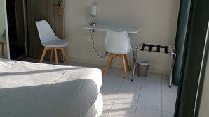 Habitación de hotel con cama, escritorio, silla, un cubo de basura y una cortina.