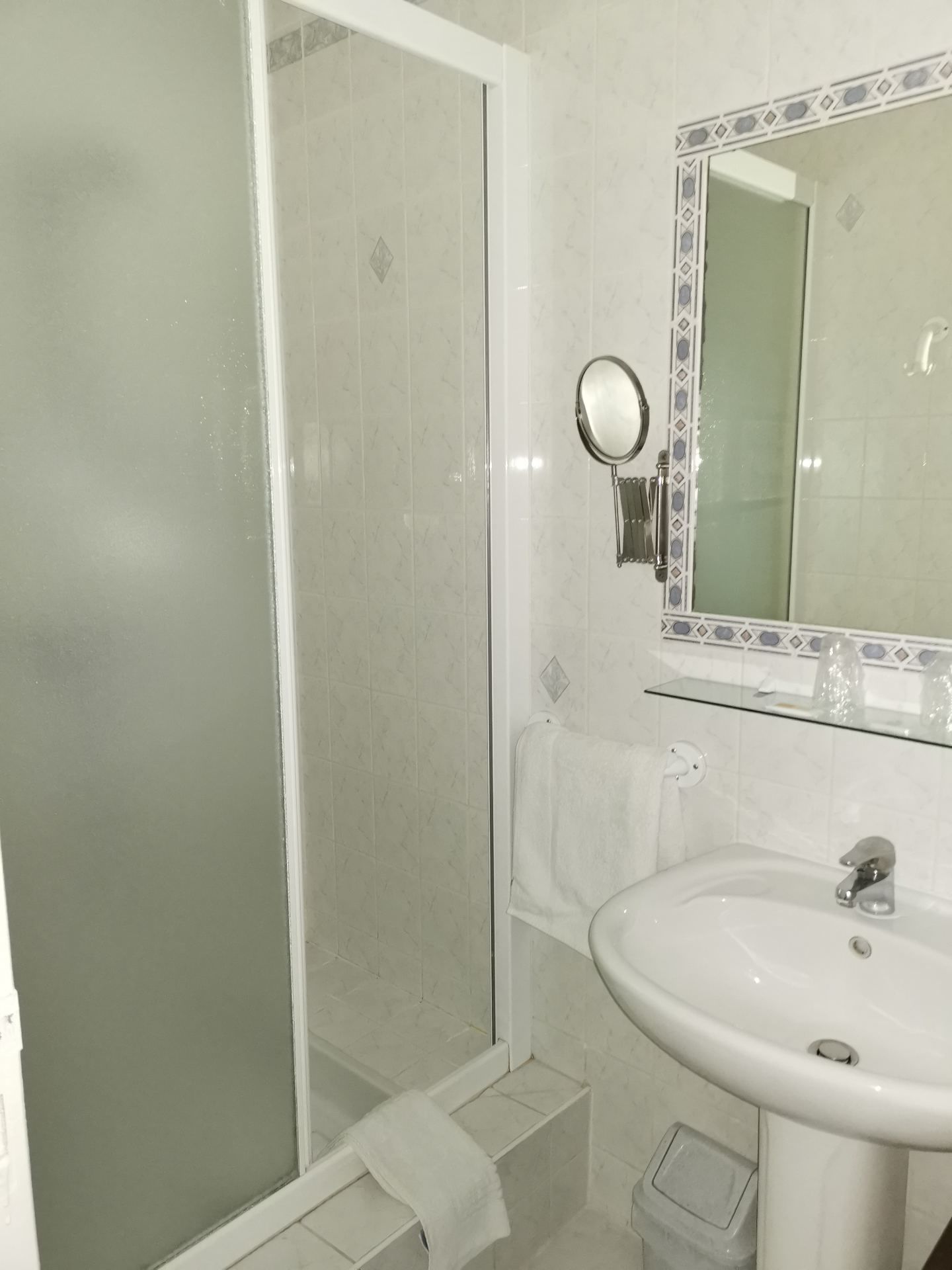 Ein Badezimmer mit Duschkabine aus Glas, einem weißen Waschbecken und einem Spiegel mit dekorativem Rahmen.