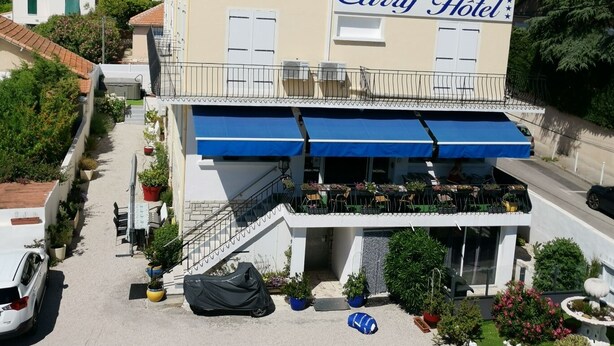 Hotel Carry, un hotel con toldo azul, mesas al aire libre y zona de estacionamiento.