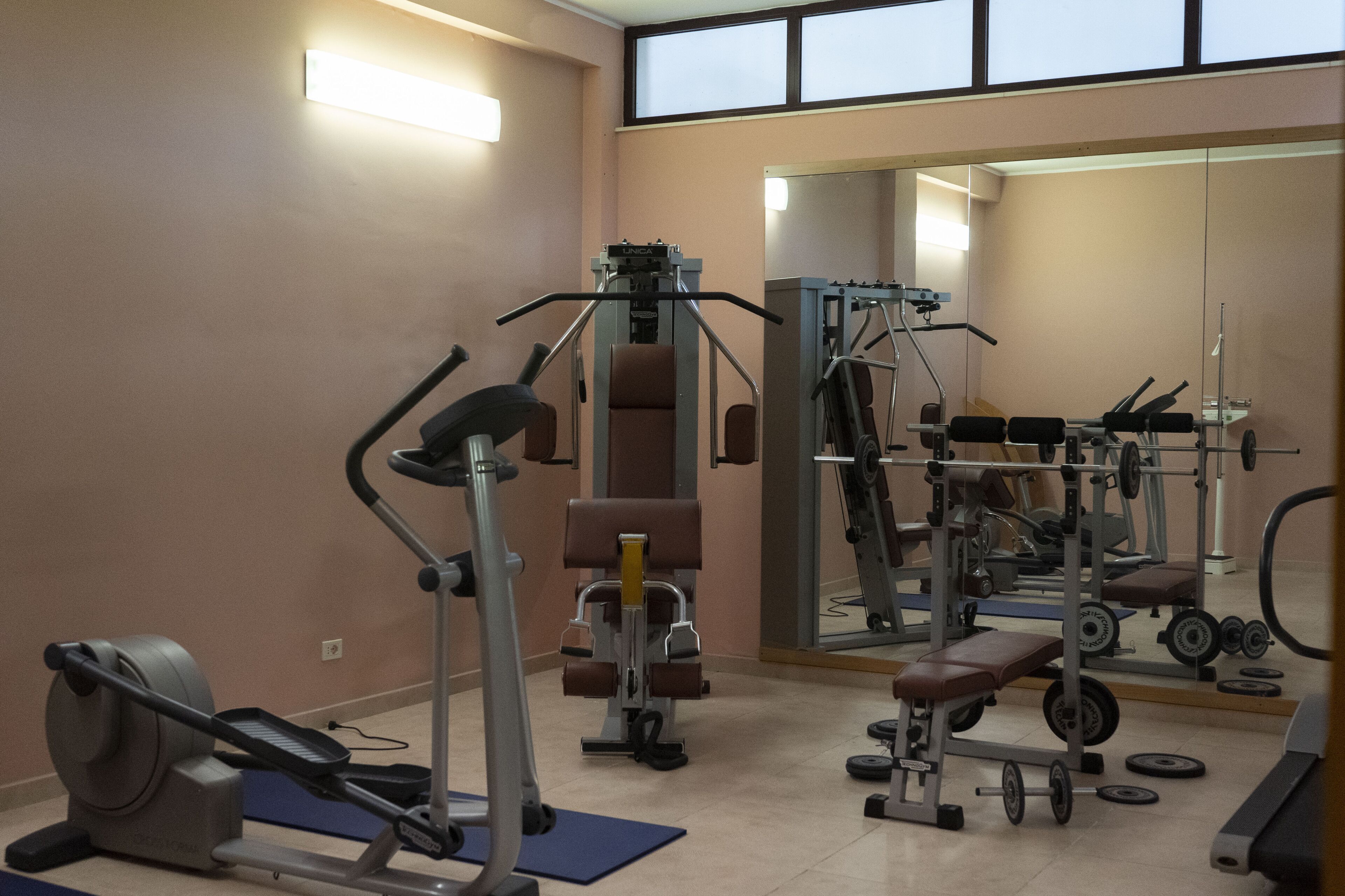 Ein Fitnessraum mit Trainingsgeräten, einem Spiegel und einem Fenster.