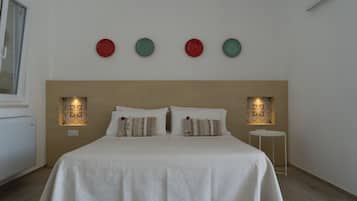 A neatly made bed with a white bedspread, two pillows, and a headboard. There are three wall-mounted lights and a small table beside the bed.