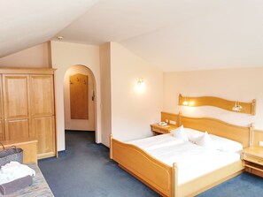 Een hotelkamer met een houten bed, nachtkastje, kledingkast en een zichtbare badkamer door een rondboogvormige deur.