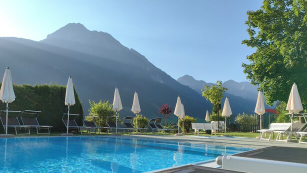 Une piscine entourée de montagnes, avec des chaises longues et des parasols.