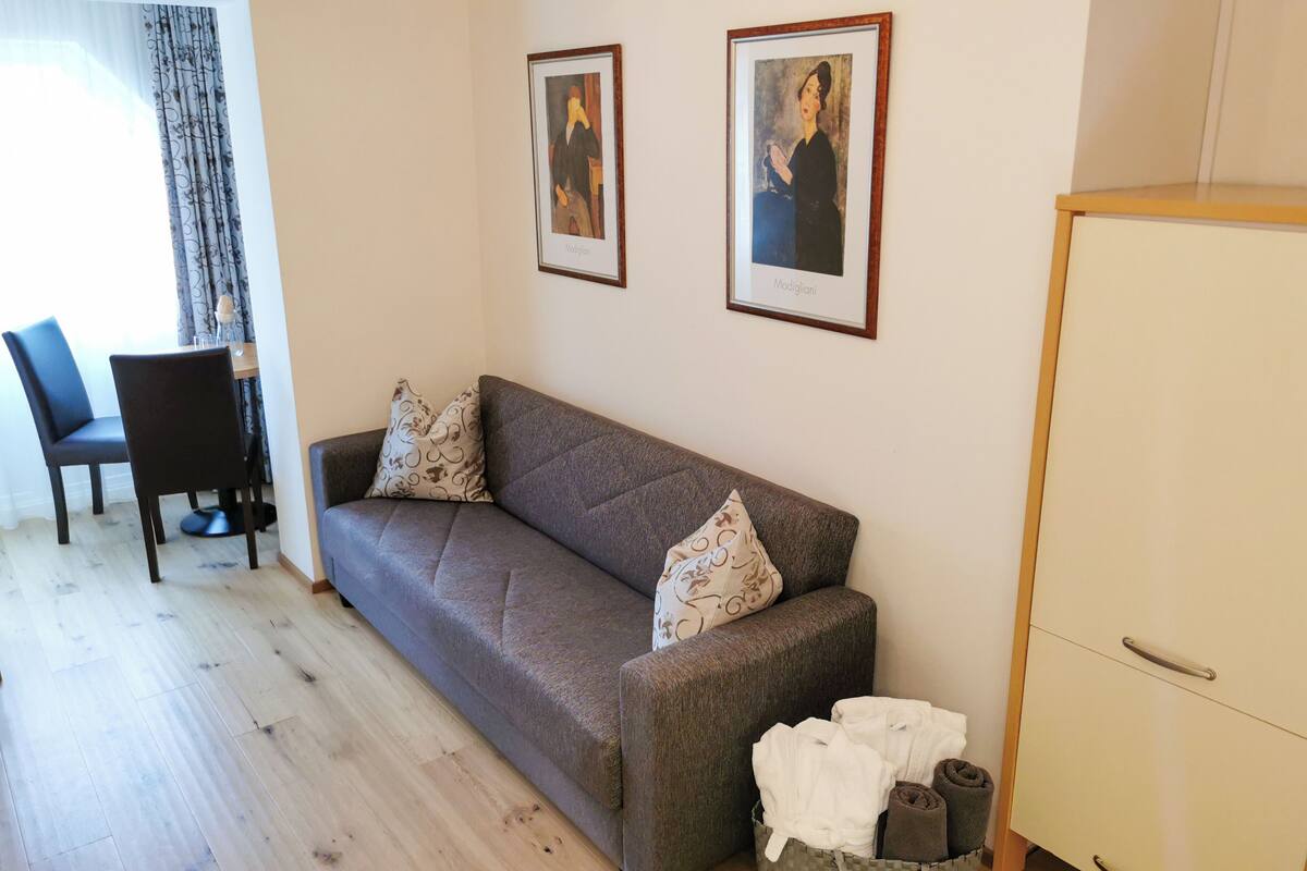 Un salon comprenant un canapé, deux fauteuils, une petite table et un meuble. Deux tableaux encadrés sont accrochés au mur.