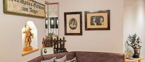 Una sala de estar con un sofá marrón, almohadones decorativos, una estatua de madera, fotografías enmarcadas y un letrero en la pared.