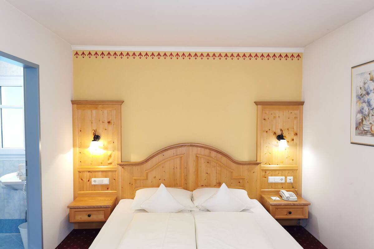 Une chambre d’hôtel avec un grand lit, une tête de lit en bois, deux tables de chevet avec des lampes et une petite table de chevet avec un téléphone.