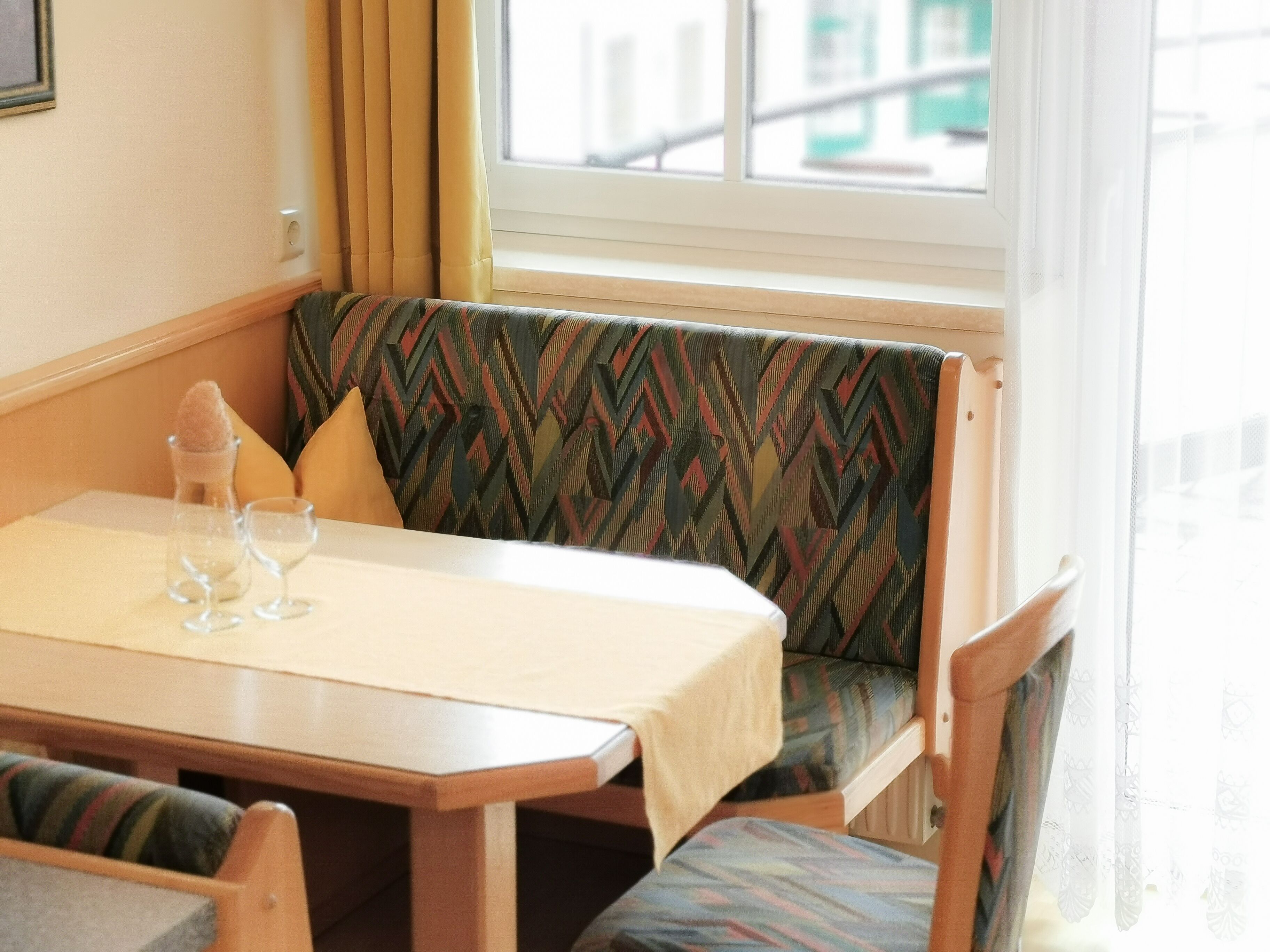 A corner seating area with a table, cushioned bench, and a window with curtains.