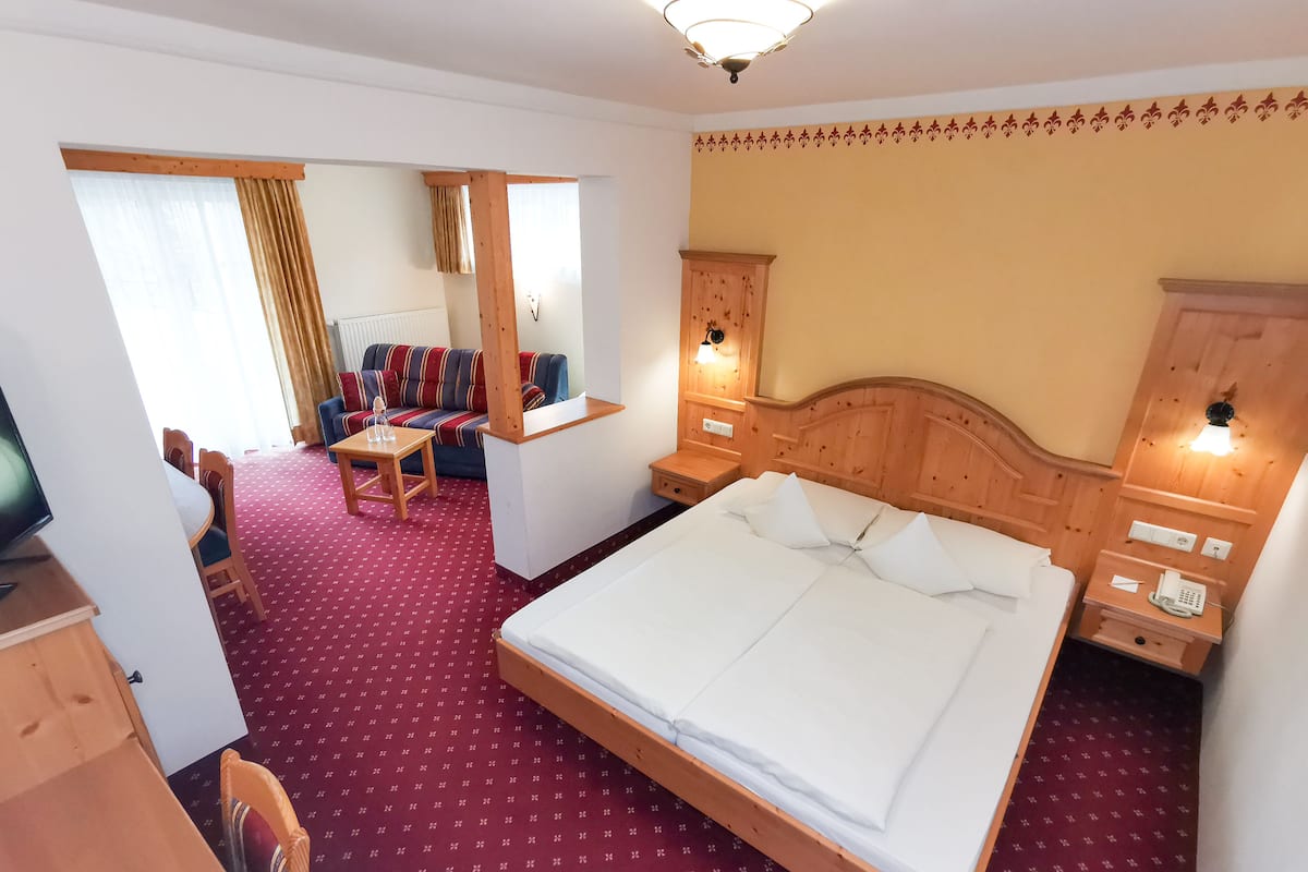 Une chambre d’hôtel avec un grand lit, une tête de lit en bois, une petite table avec une chaise, un canapé et un téléviseur.