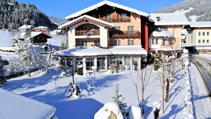 Un hôtel à plusieurs étages, dont le toit est recouvert de neige, doté d’un balcon et offrant une vue sur une montagne enneigée.