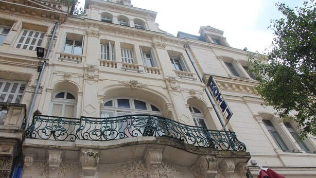 A historic building with ornate architectural details, including a balcony with decorative ironwork and a prominent entrance with a circular window. - Au Chapon Fin (Poitiers)