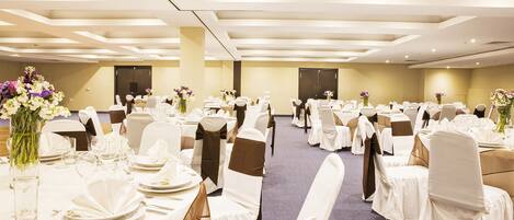 A banquet hall with round tables, white chairs, and floral centerpieces.