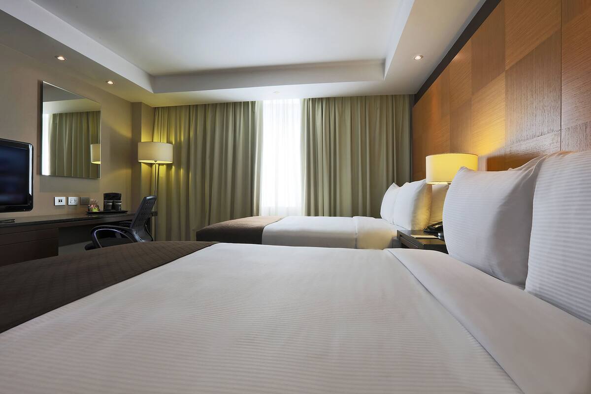 A hotel room with a large bed, a desk with a chair, a television, and a lamp.