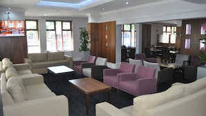 A hotel lobby with a seating area, a television, and a dining area.