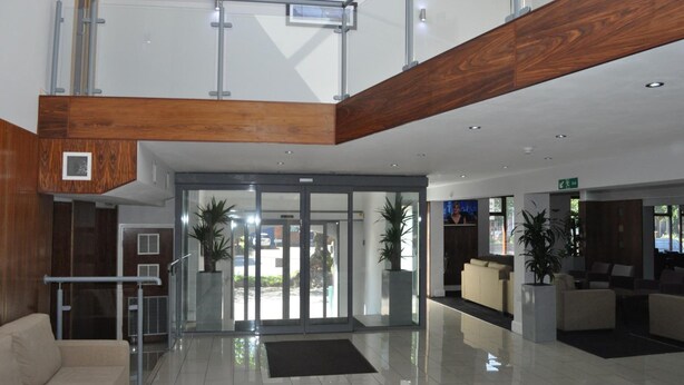 A modern lobby with a glass door entrance, a wooden ceiling, and a seating area with sofas.
