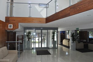 Un hall d’entrée moderne avec une porte d’entrée en verre, un plafond en bois et un espace détente avec des canapés.