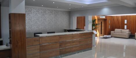 Un área de recepción moderna con un mostrador de madera, una pared con diseño y un espacio de estar con sofá y mesa de centro.