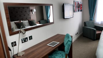 Habitación de hotel con escritorio de madera, espejo, televisor, silla estampada y cama.