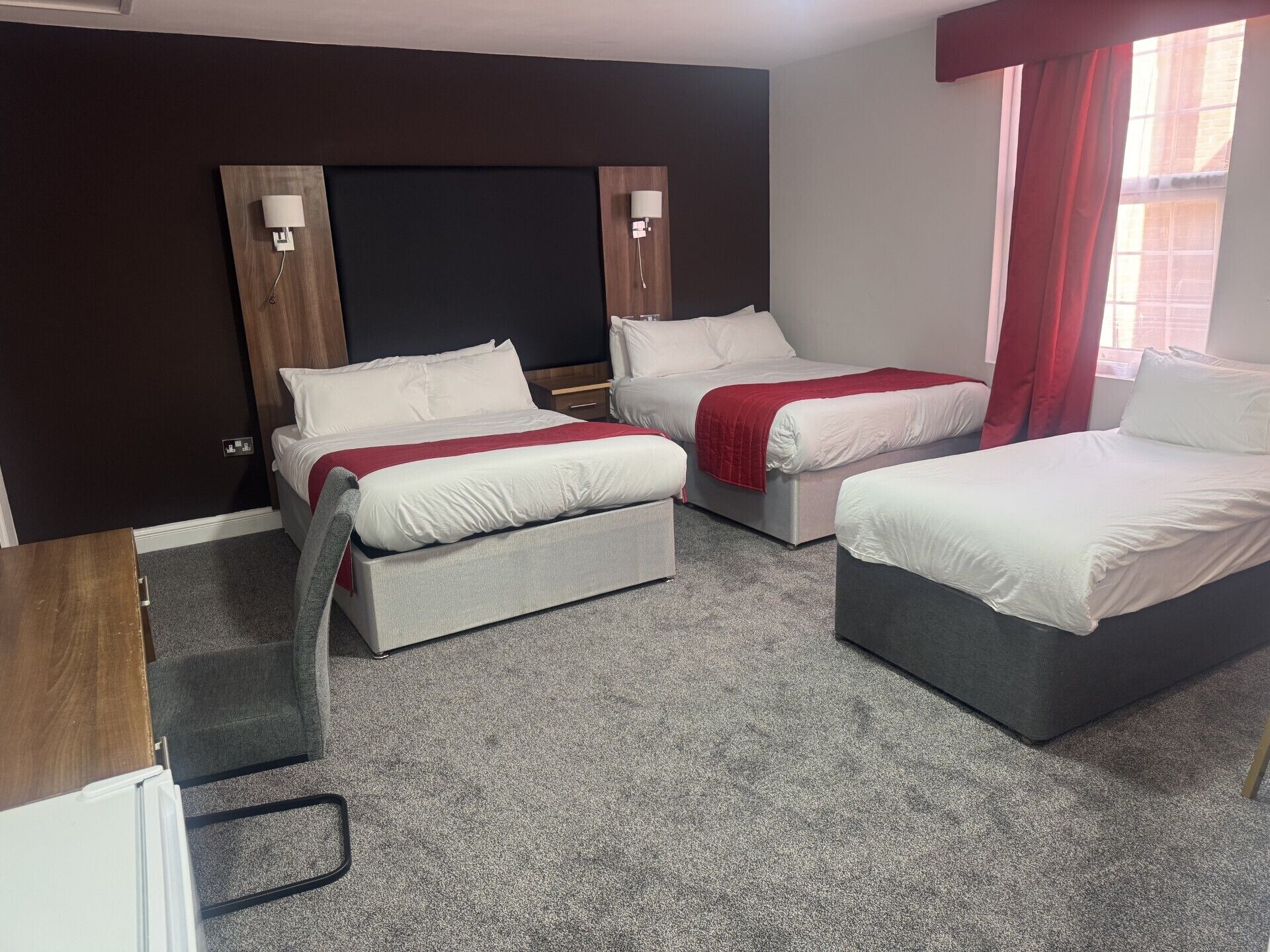 Habitación de hotel con dos camas, un escritorio y una ventana con cortinas rojas.