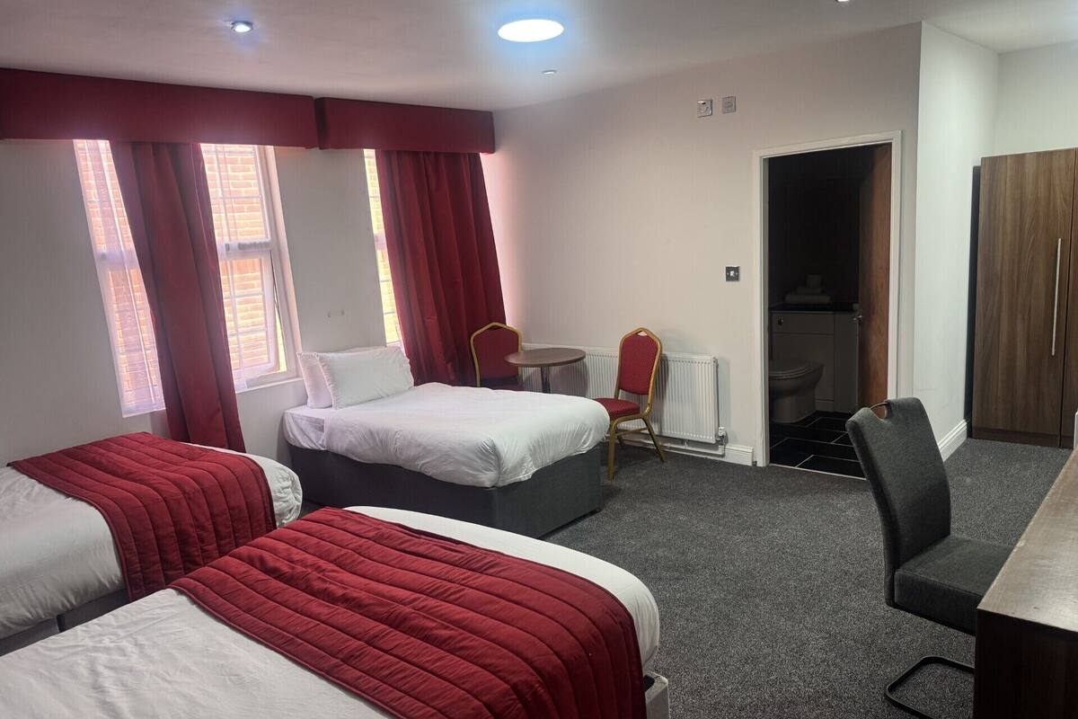 Une chambre d’hôtel avec deux lits, un bureau, une chaise et un radiateur.