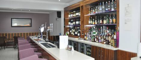 A bar area with a long counter, multiple shelves of liquor bottles, and several purple chairs.