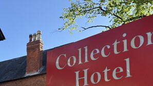 A red sign for the Collection Hotel Birmingham with a brick building in the background.