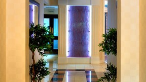 A hallway with a tiled floor, potted plants, and a decorative wall.