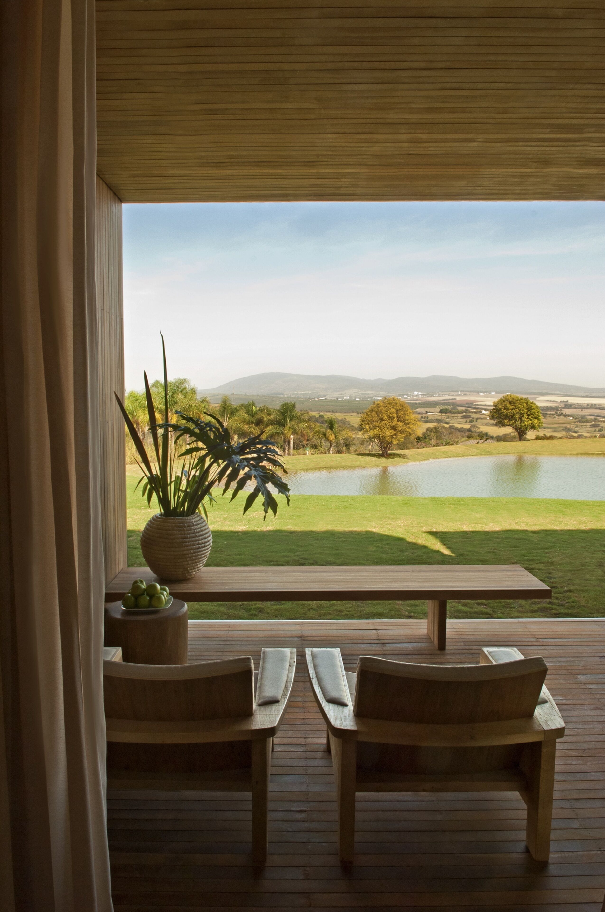 A wooden deck with two chairs and a table, overlooking a lake and distant hills.