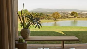 A wooden deck with two chairs and a table, overlooking a lake and distant hills.