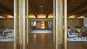 Un interior espacioso con vigas de madera, un área de estar central y vistas al exterior a través de un ventanal.