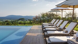 Zona de piscina con sillones reclinables y sombrillas, con vistas a un paisaje pintoresco.