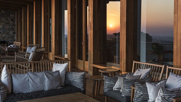 Cómoda zona de estar al aire libre con muebles de madera y cojines, con vistas a un hermoso atardecer.