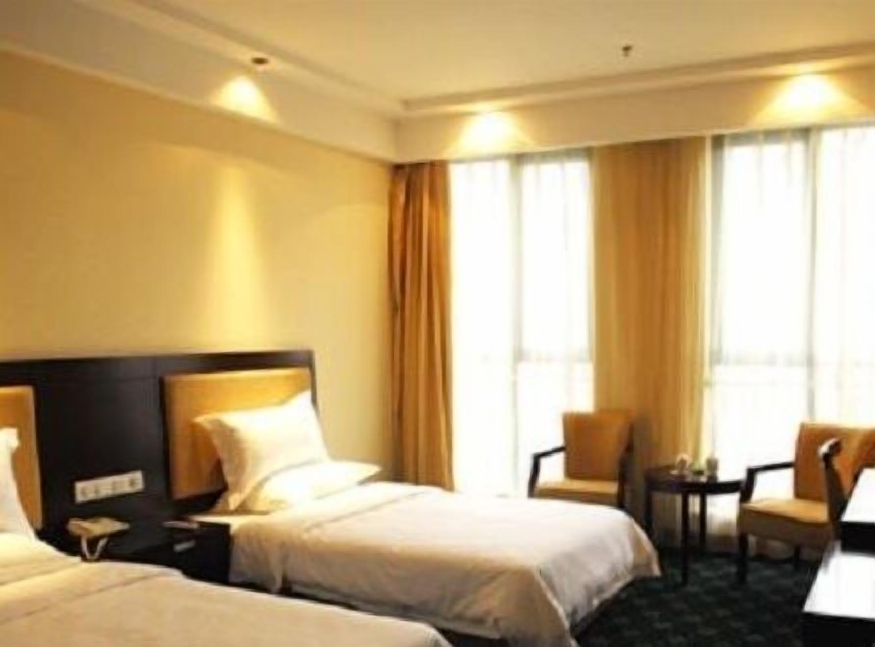 A hotel room with two beds, a small table, two chairs, and a window with curtains.