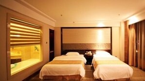 A hotel room with two beds, a large window with blinds, a bedside table, and a wall-mounted TV.