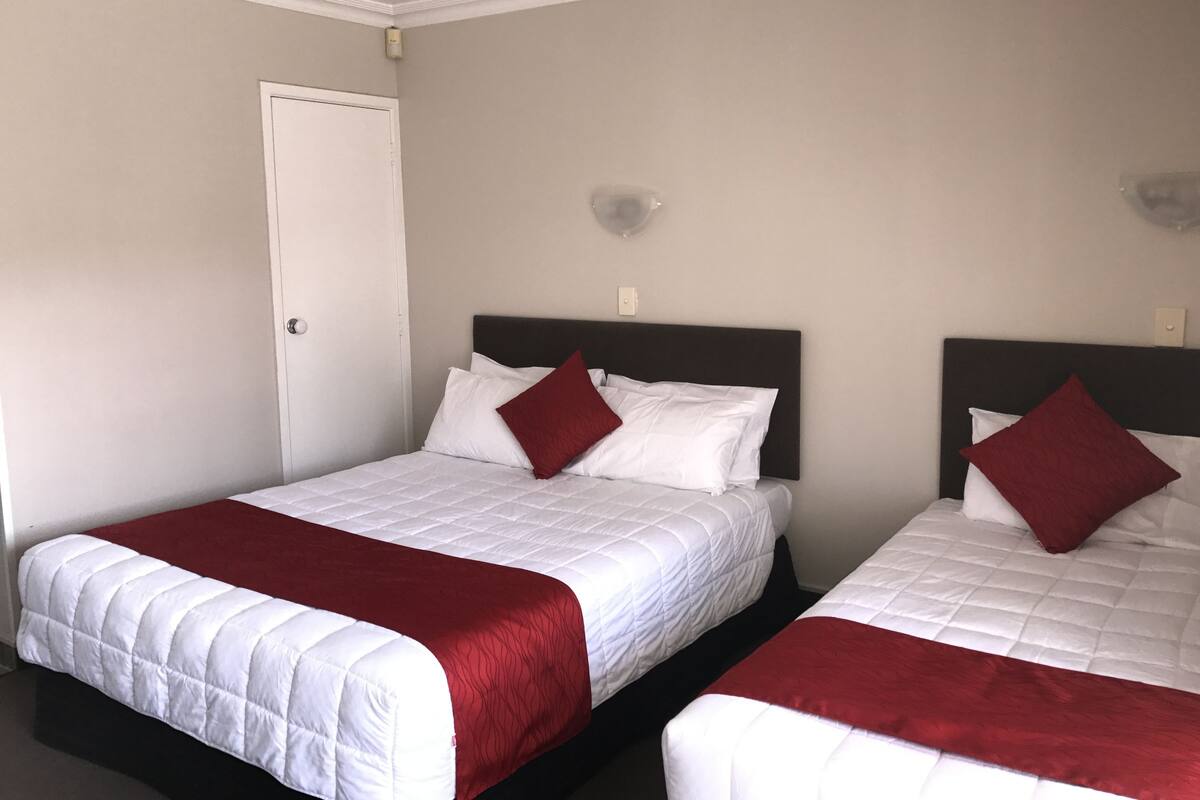 Dos camas individuales con ropa de cama blanca y roja, una puerta blanca y un interruptor de luz en la pared.