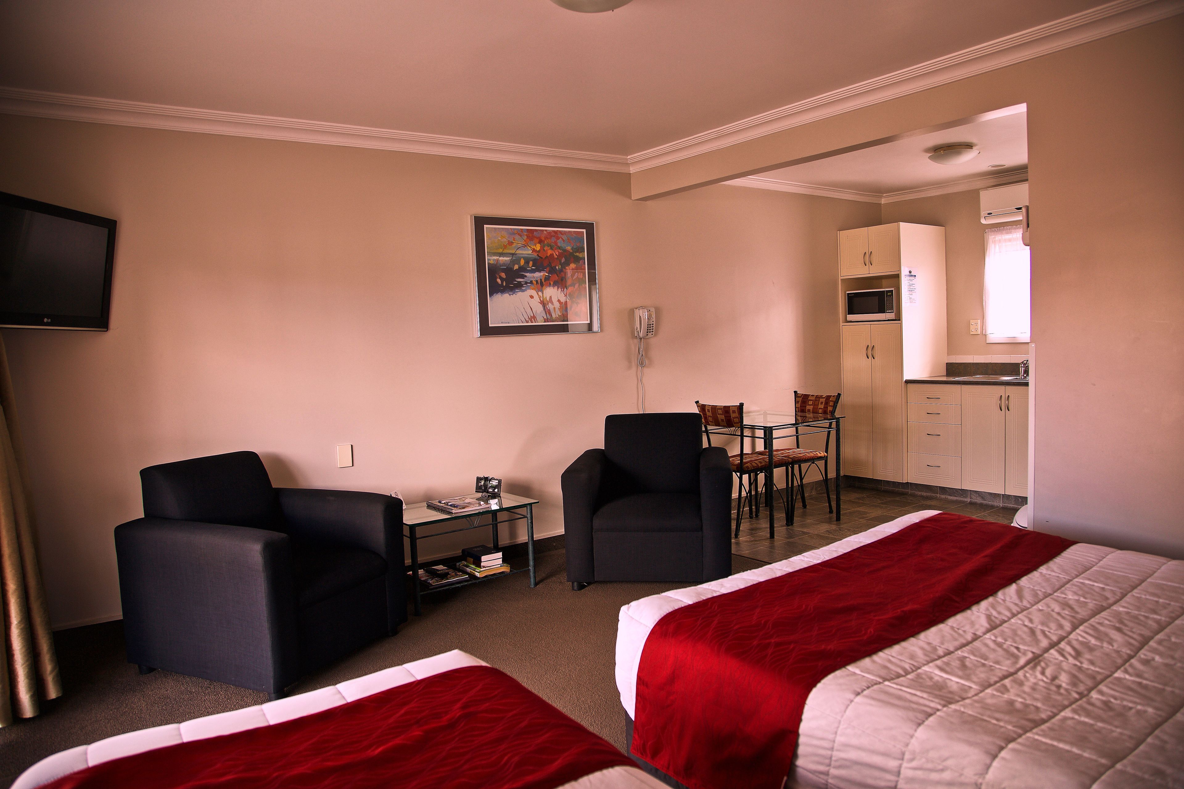 Une chambre d’hôtel avec deux lits, un bureau, une chaise, une télévision et une kitchenette.