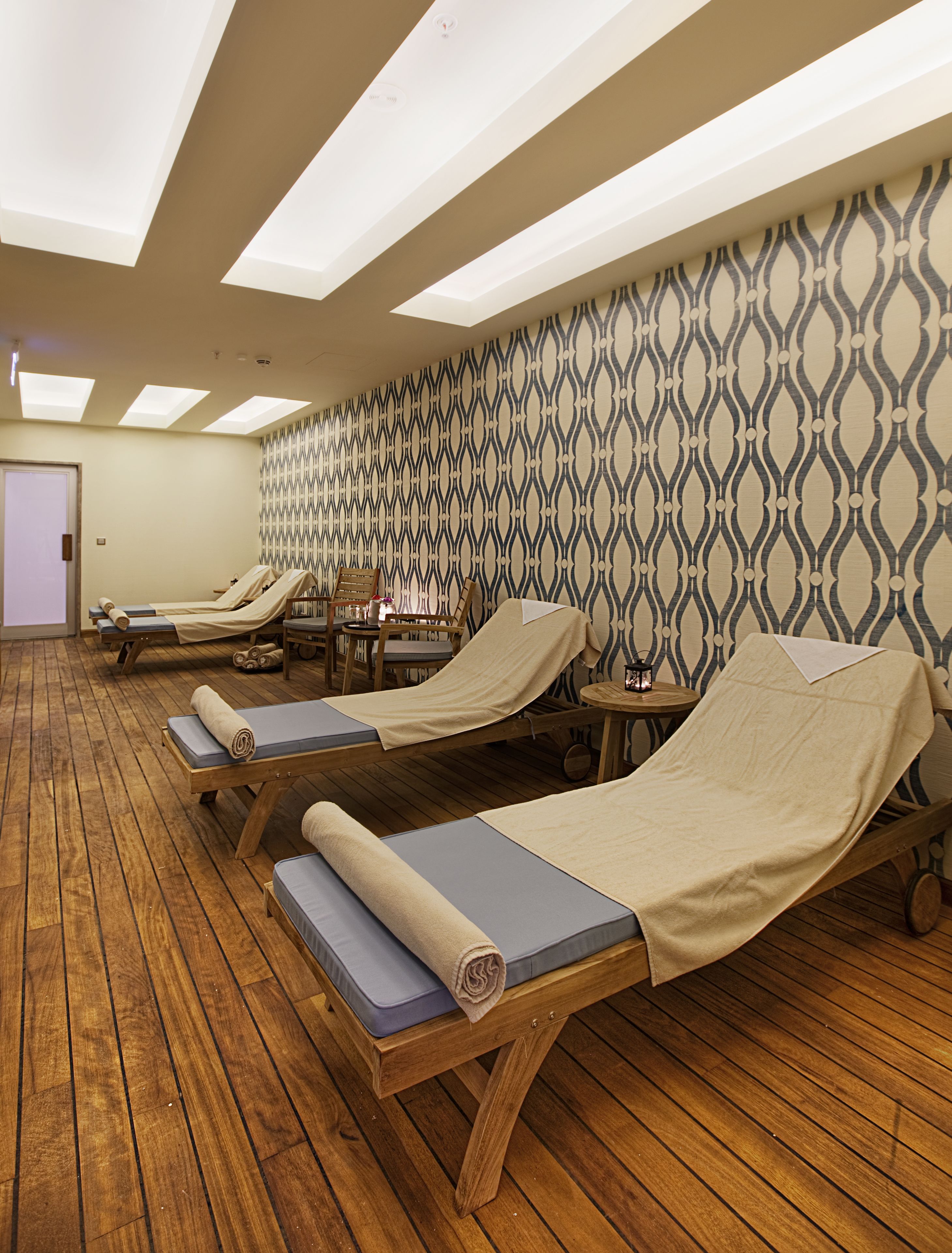 A room with wooden flooring, three reclining chairs with blue cushions, a patterned wall, and skylights.