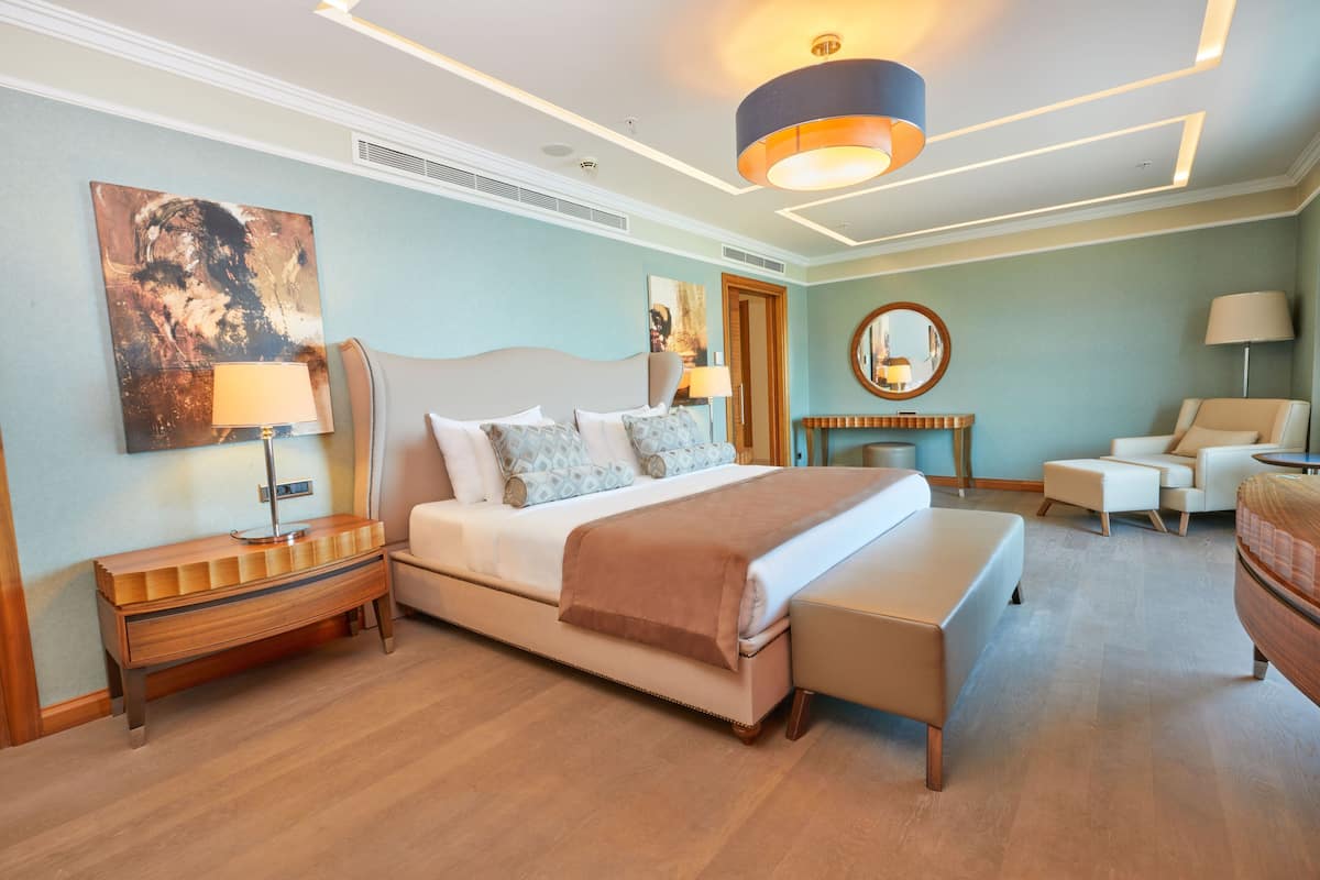 A modern hotel room with a large bed, bedside tables, a sofa, and a mirror.