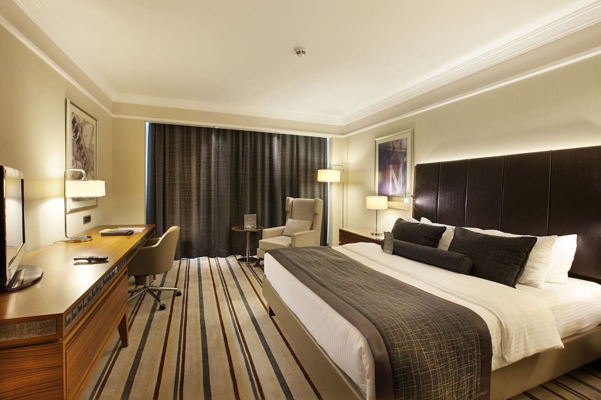 A hotel room with a large bed, a desk with a computer, a chair, and a small table.