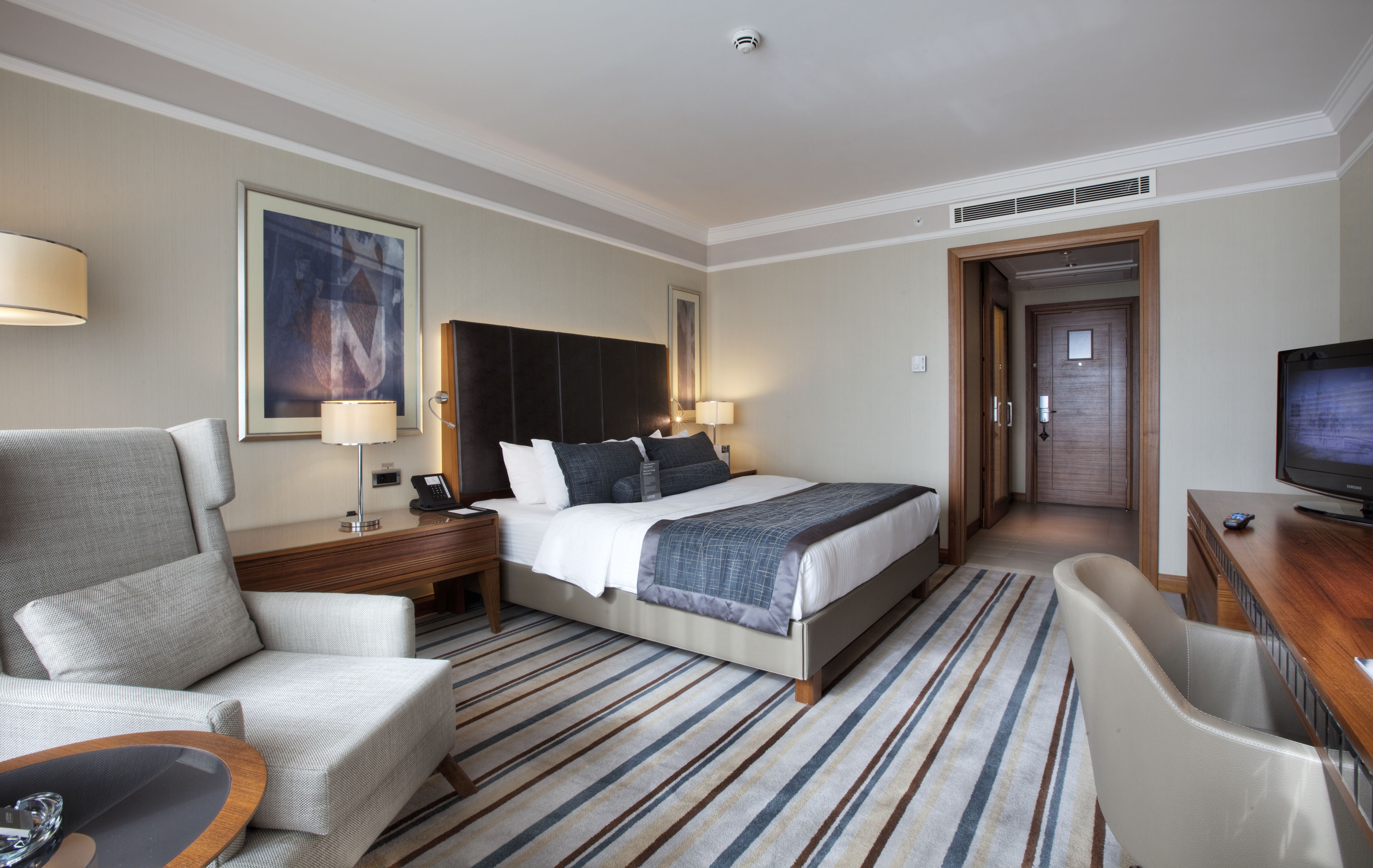 A hotel room with a bed, a desk, a chair, a TV, and a lamp.